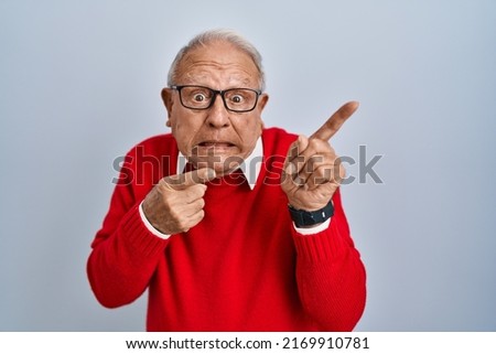 Senior man with grey hair standing over isolated background pointing aside worried and nervous with both hands, concerned and surprised expression 
