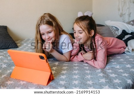 Two girls friends watch cartoons at home after school, have fun