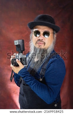 Portrait of the A long-bearded photographer wearing a black hat and sunglasses holding a vintage film camera with a flash, a vintage  photographer concepted