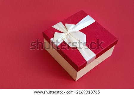 Top view of beautiful red gift box with satin light ribbon on red background. A gift for Christmas, New Year or a romantic Valentine's Day. Copy space for text.