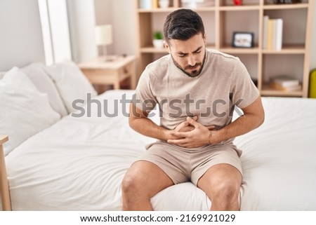 Young hispanic man suffering for stomachache sitting on bed at bedroom Royalty-Free Stock Photo #2169921029