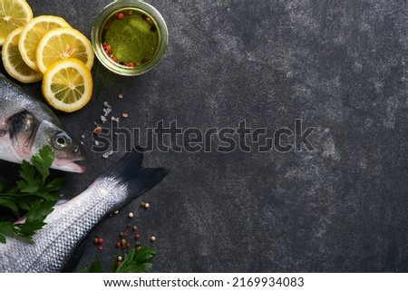 Sea Bass raw. Fresh sea fish bass with salt, pepper, parsley, olive oil and lemon on dark concrete rustic background. Fresh fish ready to cook. Food cooking background. Top view, copy space.
