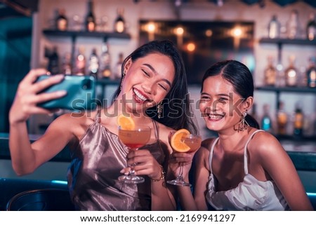 Two lovely ladies taking a selfie while having fun at a bar and having cocktails. Ordered tequila sunrise and posting it to social media. Friends bonding at the nightclub.