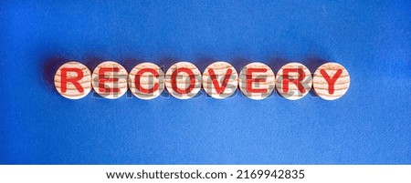 The word 'recovery' on wooden circles on blue table. Beautiful background, copy space.