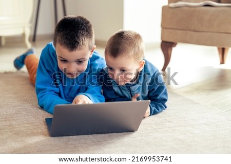 Boys watching cartoons on laptop at home in living room.