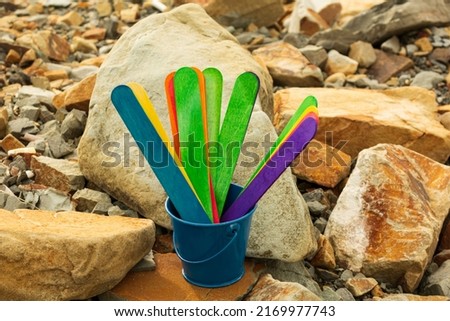 Colorful wooden sticks inside of a blue bucket with stone beach background. Bucket list concept.