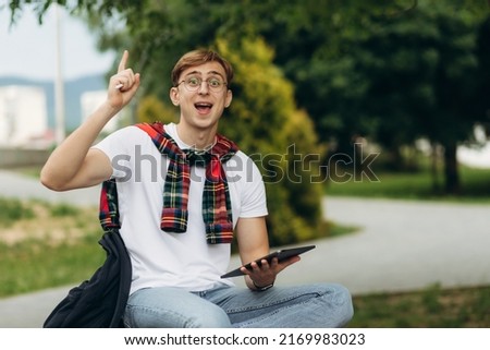 Happy smiling student outdoors with tablet. Emotion of joy. The guy has an idea. The concept of college education