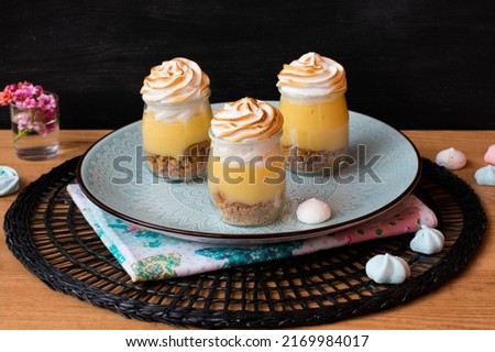 Lemon pie dessert served in glass on blue plate, wooden table and black background