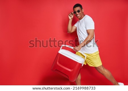 Happy African man carrying cooler box while walking against red background         