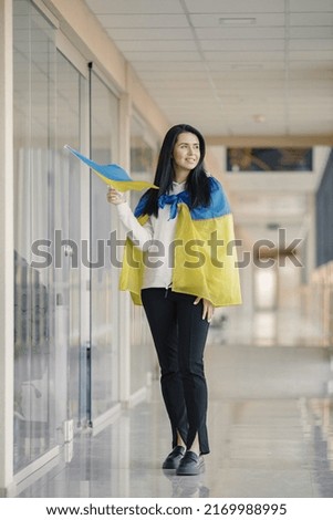 Brunette young woman with big Ukrainian flag standing and posing for a photo