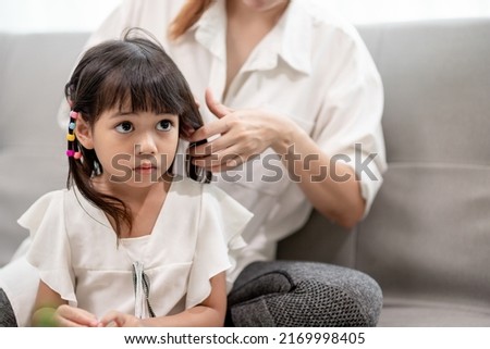 Young Asian mother tying daughter's hair