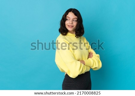 Teenager Ukrainian girl isolated on blue background with arms crossed and happy