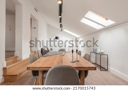 Dining room with natural wood table with steps leading to another room, skylights in the sloping ceiling and fabric upholstered chairs Royalty-Free Stock Photo #2170015743
