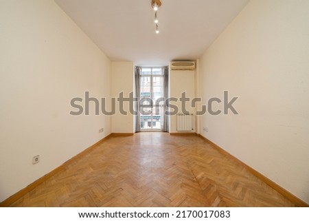 An empty room with light cream painted walls, herringbone oak parquet floor, balcony with curtains and white aluminum radiators