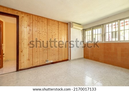Empty room with walls covered in pine tongue-and-groove, windows on one wall and air conditioner