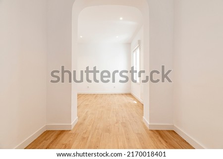 Empty room with plain white painted walls, plain aluminum windows and basket-handle arch separating the rooms with light oak wood floors