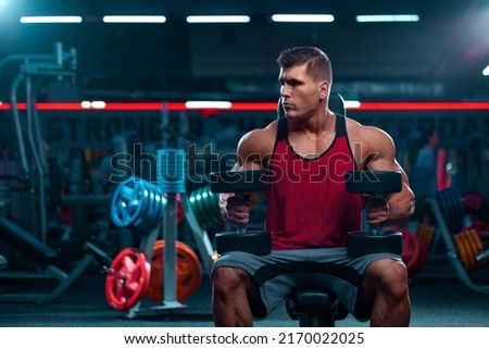 Bodybuilder athlete man with dumbbells pumping up muscles in the gym. Brutal strong muscular guy on fitness workout. Bodybuilding concept. Royalty-Free Stock Photo #2170022025