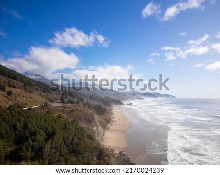 Beautiful seascape. Ocean coast. Light waves crash on the sandy shore. Green forest on the hill. Blue sky with white clouds. There are no people in the photo. Advertising of tourist destinations.