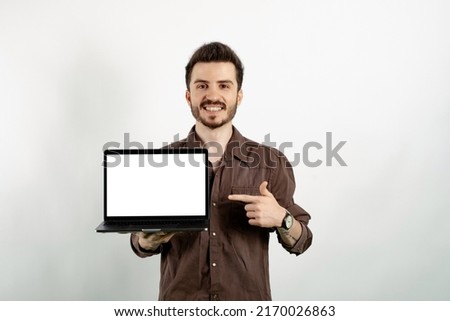 Young man smiling confident wearing casual clothes posing isolated over white background pointing with index finger to laptop pc computer with blank empty screen
