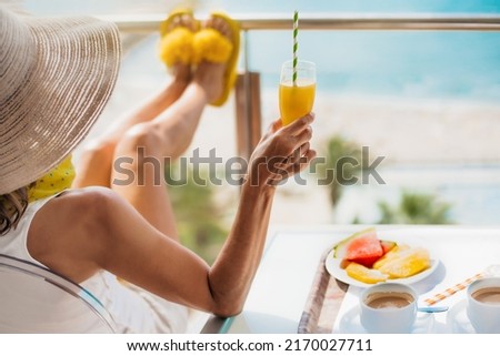 detail of a middle-aged woman with straw hat having breakfast on the terrace of a hotel and contemplating the sea. concept of relaxation and summer vacations in the mediterranean.