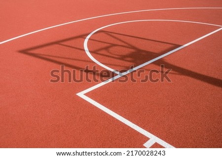 Shadow of the rack with shield and basketball ring on orange basketball rubber field ground during sunny day outdoors. Basketball game background Royalty-Free Stock Photo #2170028243