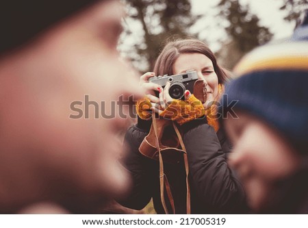 Woman with vintage camera is taking picture of her little son and husband outdoor