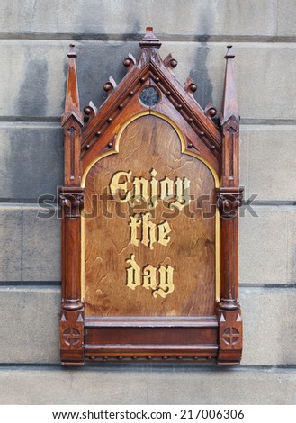 Decorative wooden sign hanging on a concrete wall - Enjoy the day
