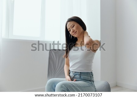 Neck ache. Tormented from fibromyalgia tanned beautiful young Asian woman rubbing massaging tensed muscles at home interior living room. Injuries Poor health Illness concept. Cool offer Banner