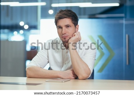 Portrait of a young male student. Serious, preparing for the exam, studying online, remotely. Sitting at the table with a laptop, tired, holding his head in his hand