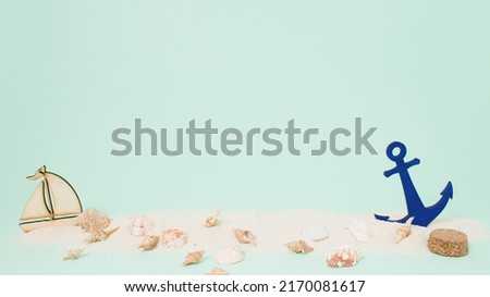 Bright sea sand decorated with shells, anchor and boat on pastel green background. Minimal summer concept. Perfect summer party or peaceful ocean aesthetic with copy space.