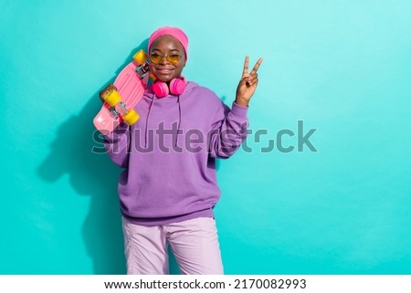 Portrait of attractive cheerful girl holding skate showing v sign isolated over bright teal turquoise color background
