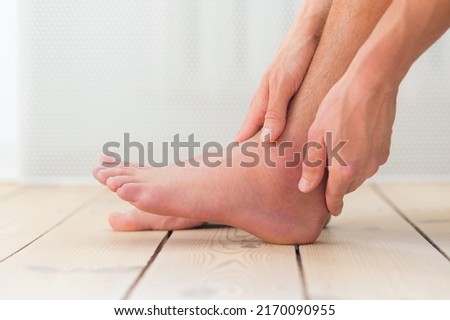 Sprained and swollen ankle. Man hold his sprained ankle sitting on the sofa at home. Ankle sprain. Injury. Royalty-Free Stock Photo #2170090955