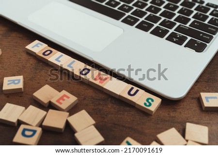Follow Us. Wooden board game letter puzzles on a wooden table next to silver laptop. Advertisement gaining clients and followers. High quality photo