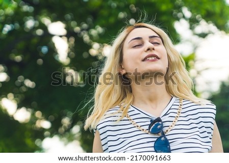 blond Caucasian girl enjoying fresh air in summer. medium closeup natural green background. High quality photo