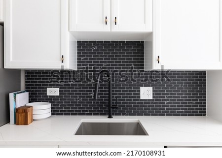 Kitchen sink detail shot with white cabinets, small black marble subway tile backsplash, and a black faucet. Royalty-Free Stock Photo #2170108931