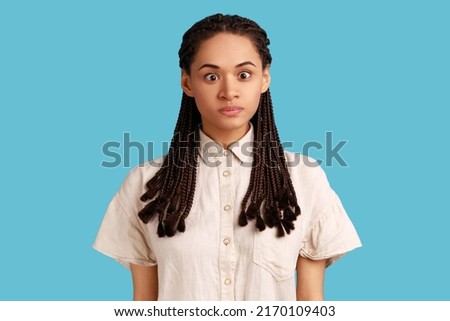 Portrait of funny silly woman with black dreadlocks looking at camera, cross eyed with stupid dumb face, has awkward confused comical expression. Indoor studio shot isolated on blue background.