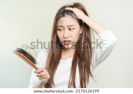 Serious, worried asian young woman, girl holding brush, show her comb, hairbrush with long loss hair problem after brushing, hair fall out on her hand in living room. Health care, beauty treatment. Royalty-Free Stock Photo #2170126199