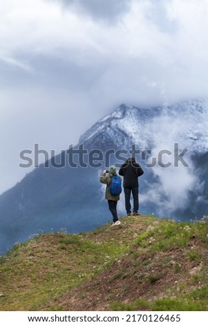 Tourists take pictures of the beautiful mountain snowy peaks of the Eastern Sayan Mountains covered with low clouds. Traveling in the highlands, outdoor activities