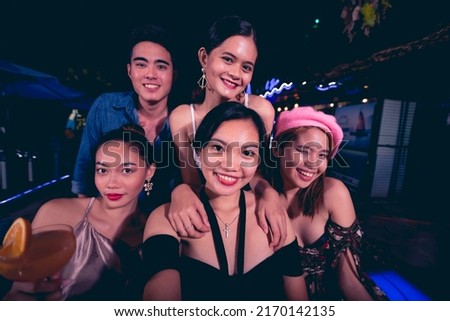 Five young friends take fun selfies while partying at a nightclub or bar. 5 people having a great time together. Nightlife scene.
