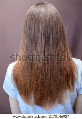 A girl with long, straight and beautiful brown hair. Hair care at home. Hair regrowth after hair coloring with henna. Back view