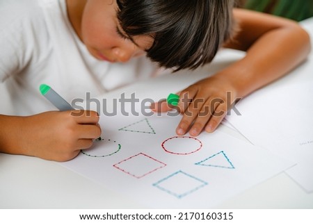 Preschooler boy sitting at the desk, drawing shapes  Royalty-Free Stock Photo #2170160315