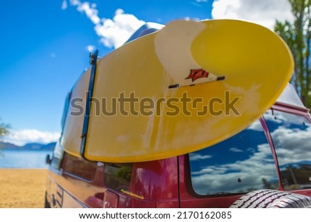 Camper van with colorful surf board on a sunny summer day at the beach. Vintage car parked on the beach or seaside with a surfboard on the side. Leisure trip in the summer. Travel photo, nobody