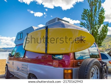 Camper van with colorful surf board on a sunny summer day at the beach. Vintage car parked on the beach or seaside with a surfboard on the side. Leisure trip in the summer. Travel photo, nobody Royalty-Free Stock Photo #2170162943
