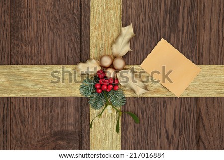 Christmas background with gold ribbon, holly, fir, mistletoe and bauble decorations with gift tag over old oak.