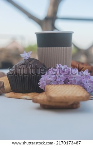 Chocolate cupcake, cookies, take away cup of coffee and lilac flowers, outdoor photo