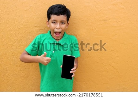 Latin child boy over isolated yellow background with cell phone in victory position shows happy and excited	