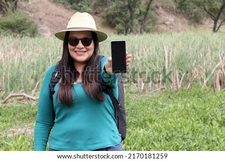Latin adult woman with hat and sunglasses is in the middle of the forest using his cell phone to send and receive messages and search the location on the map	