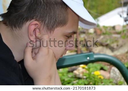 An autistic guy sits with his fingers covering his ears, autistic behavior traits Royalty-Free Stock Photo #2170181873