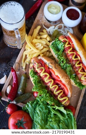 BBQ hot dog served with vegetables and French fries and sauces on wooden serving board