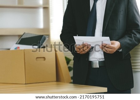 Resignation. The businessman puts his box of his belongs on the desk and holds the white letter. Quitting a job, a businessman fired or leave a job concept. The great Resignation.
 Royalty-Free Stock Photo #2170195751